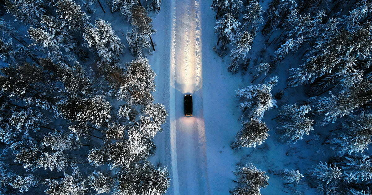 Drönarbild bil kör på vinterväg genom snötäckt skog i Norrland